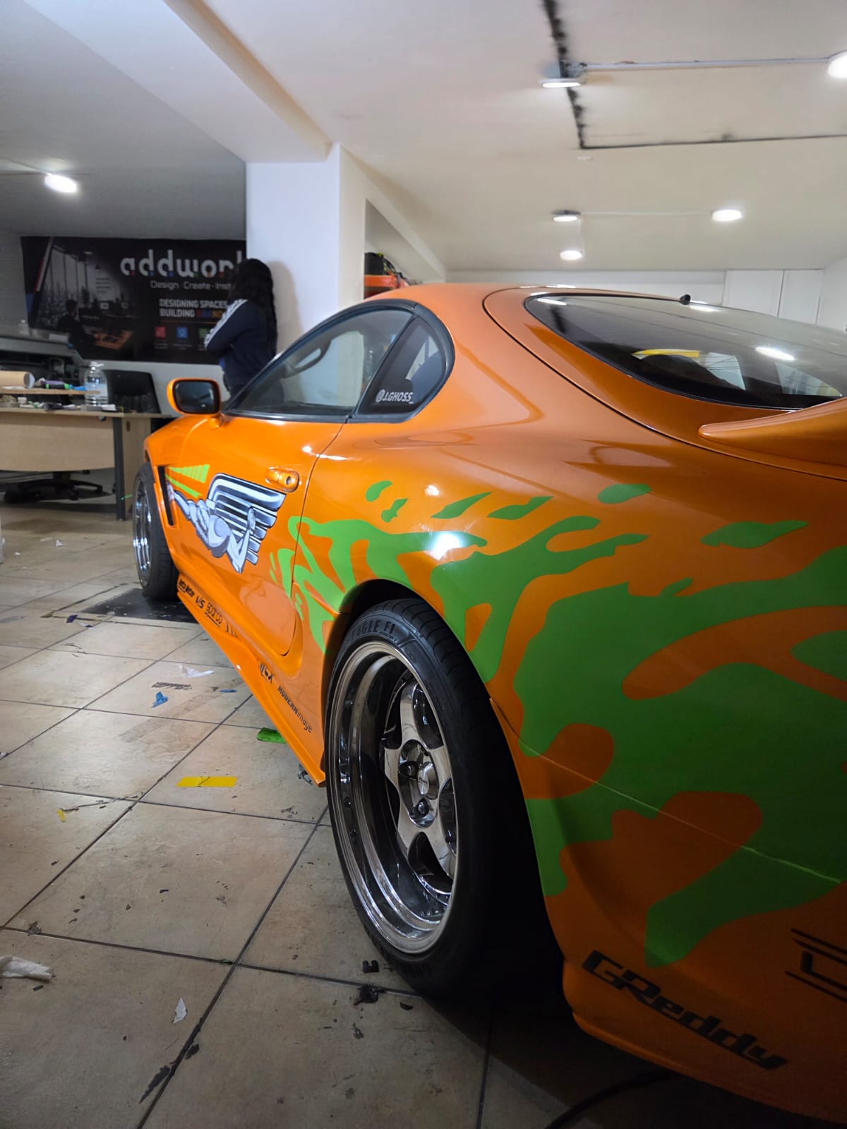 Orange sports car with green flame-style vinyl graphics in the Addworks workshop